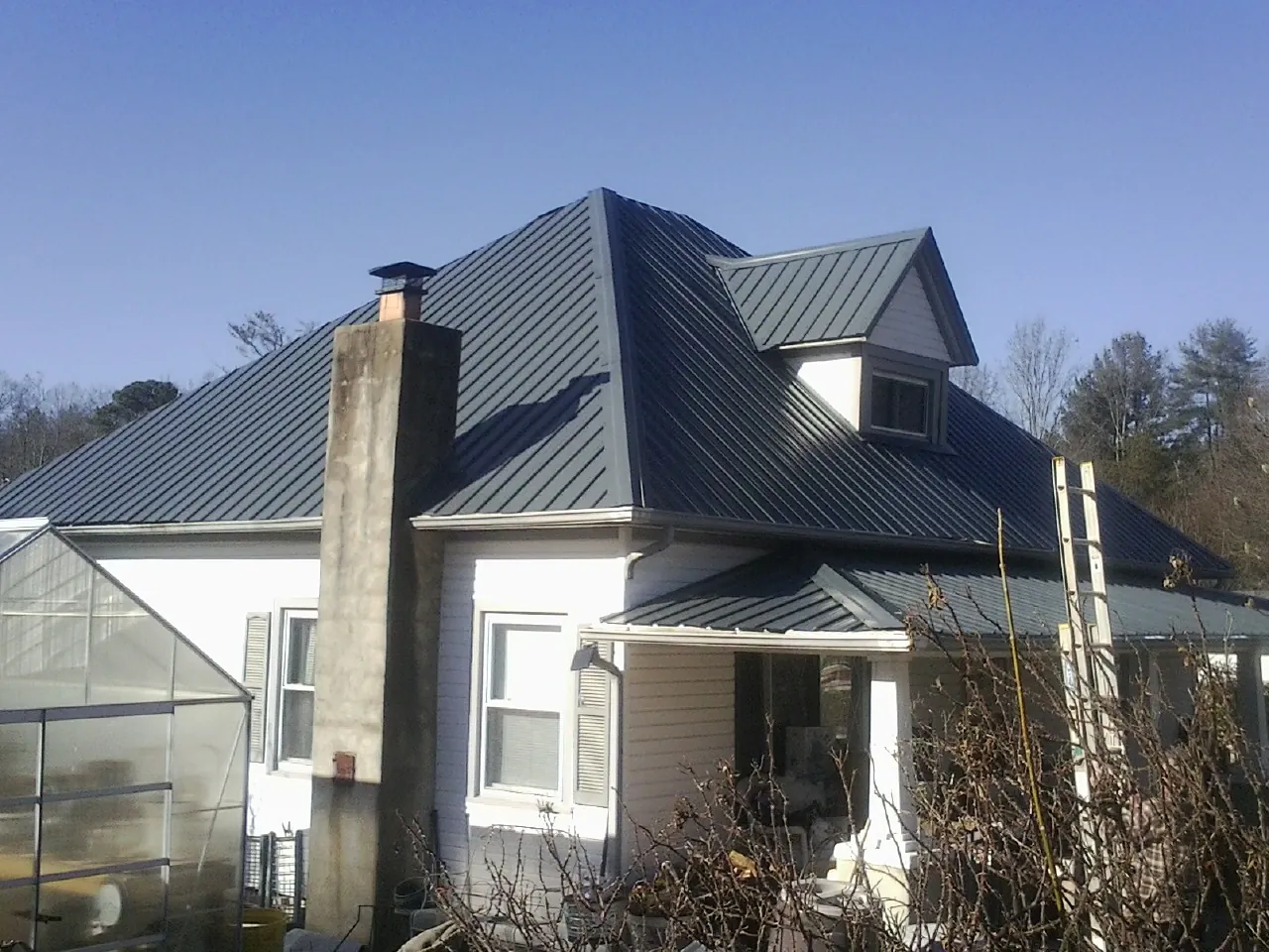 Dark blue standing seam metal roof on a white farmhouse with dormer — Slate & Tile Roof Repair by Roofing Brothers in Sweeden