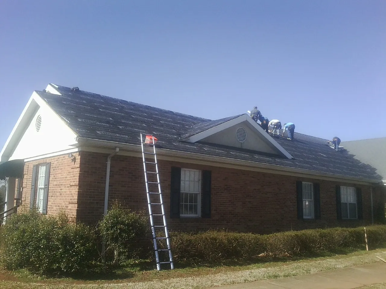 Crew tearing shingles off a brick ranch roof with a ladder set — Emergency Roof Repair work by our crew in Sweeden