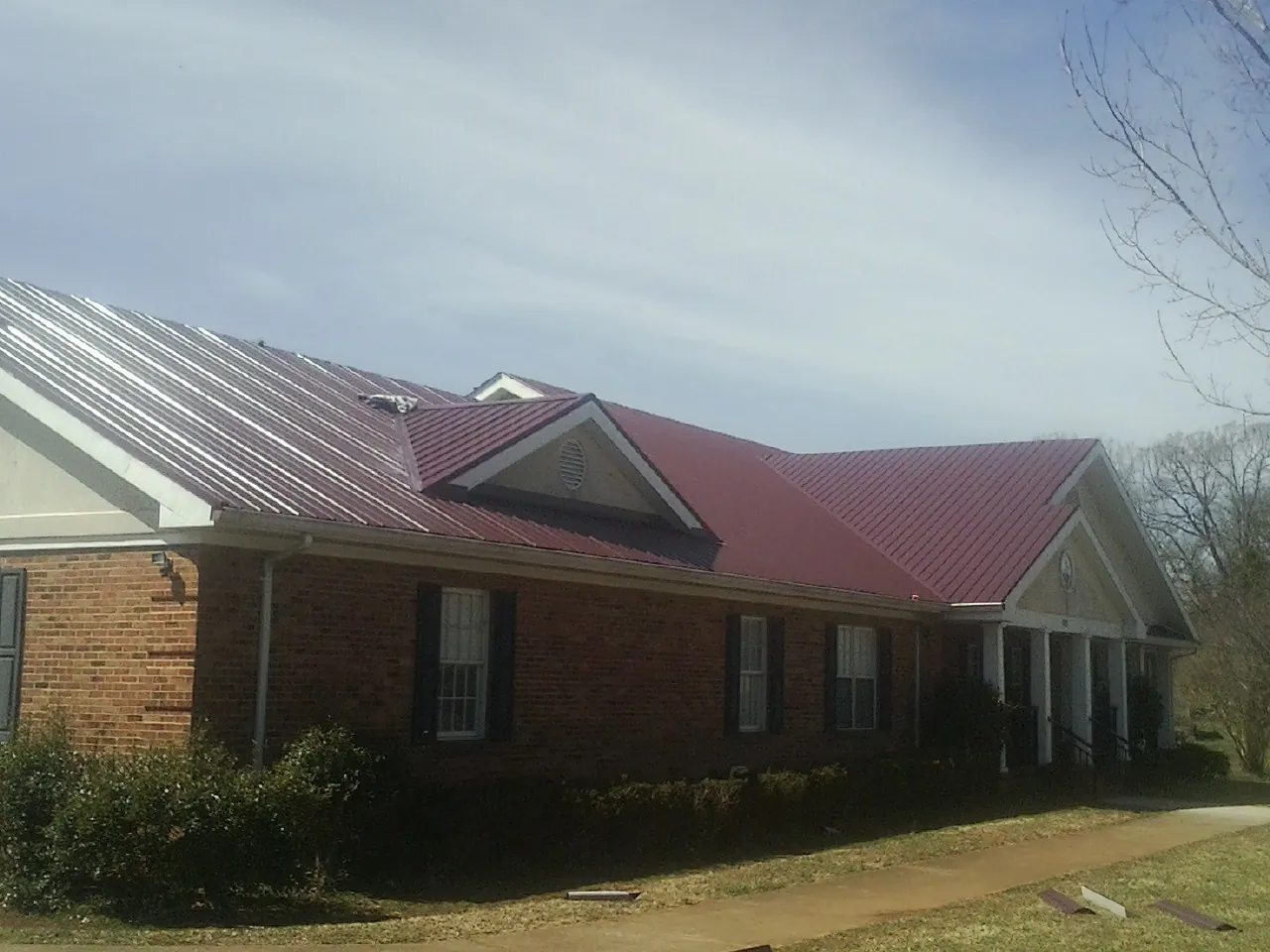 Red metal roof with gabled entries on a long brick building, from a Hail Damage Roof Repair job in Sweeden