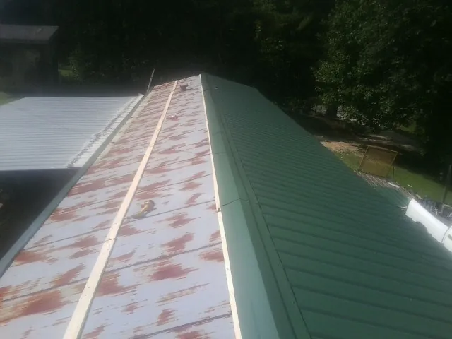 Old rusted panels beside newly installed green metal roofing — Wind Damage Roof Repair by Roofing Brothers in Sweeden