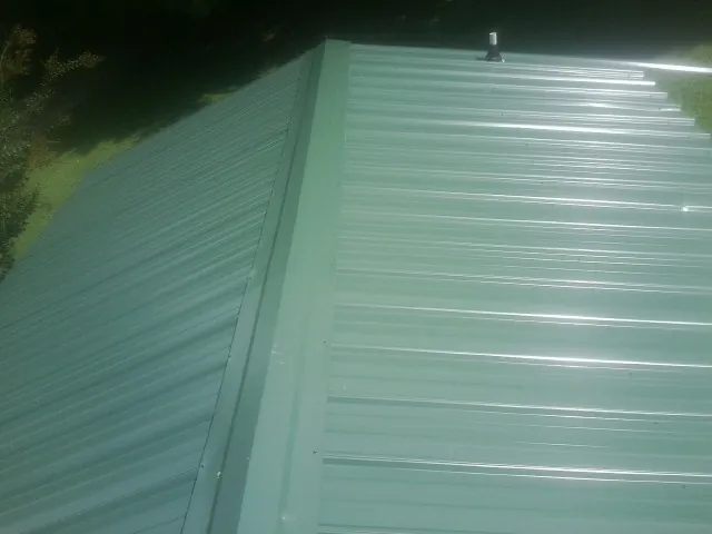 New green metal panels meeting at the ridge of a roof — Flat Roof Repair work by our crew in Sweeden