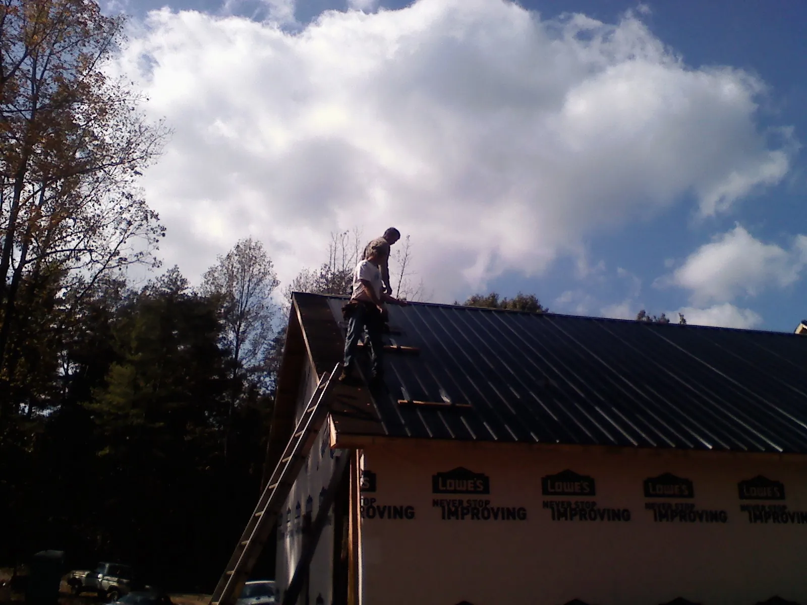 Roofer fastening dark metal panels high against a cloudy sky, from a Roof Inspection job in Sweeden
