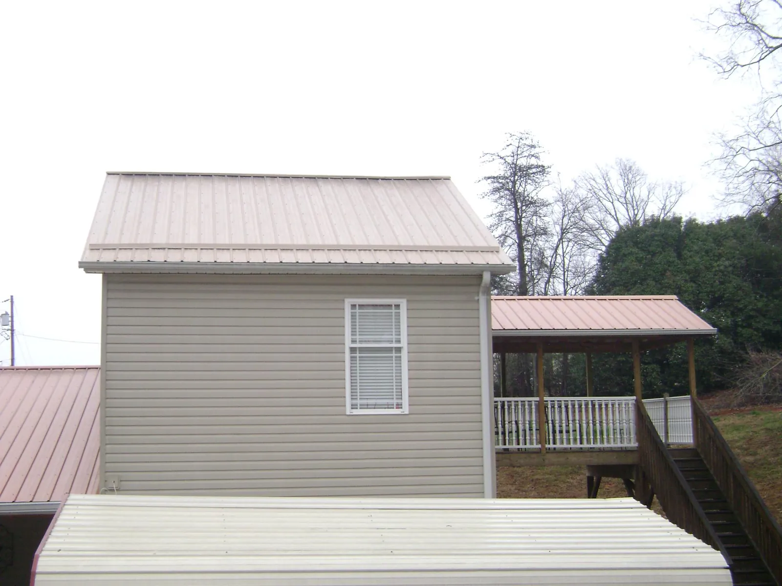 Tan metal roofs on a two story addition and attached porch, from a Roof Replacement job in Sweeden